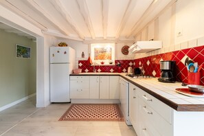 A kitchen with white cabinets, a red and white tiled backsplash, a built-in stove, and a refrigerator. - La Maison Maudanaur - Maison familiale avec jardin (Morainville-Jouveaux)