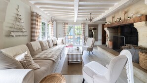 A spacious living room with a long sofa, a fireplace, and a view through large windows. - La Maison Maudanaur - Maison familiale avec jardin (Morainville-Jouveaux)