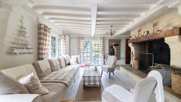 A spacious living room with a long sofa, a fireplace, and a view through large windows.