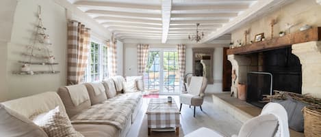 A spacious living room with a long sofa, a fireplace, and a view through large windows.