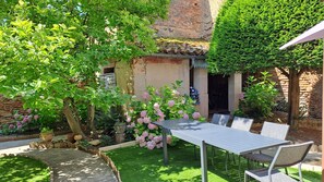 Un espace patio aménagé avec une table et des chaises, entouré d’une végétation luxuriante et de plantes en fleurs.