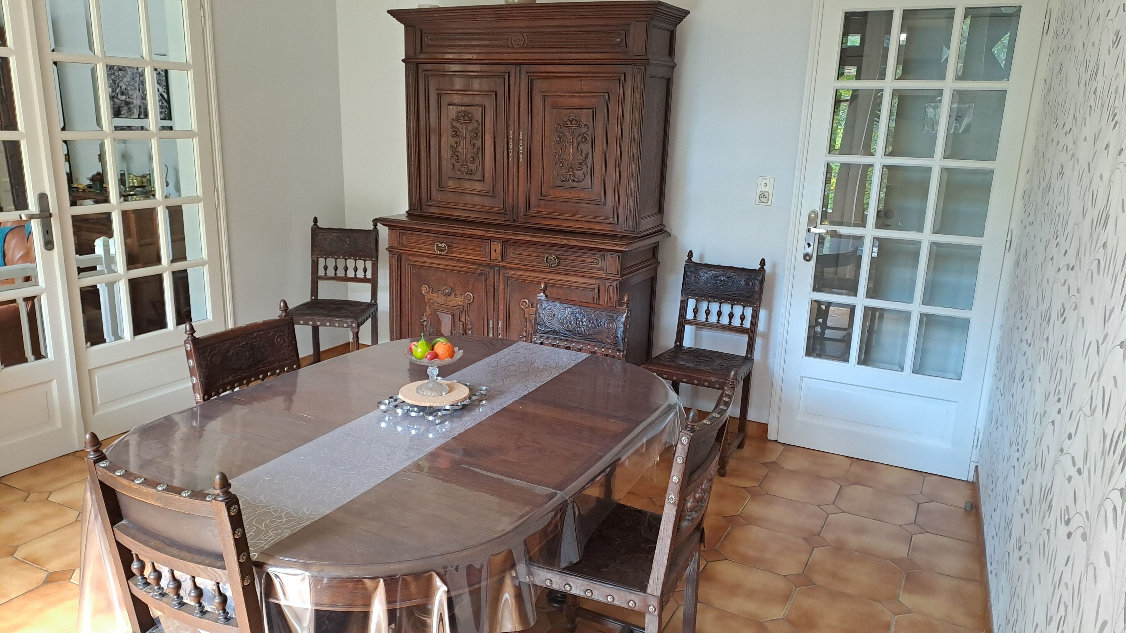Un coin repas avec une table en bois, des chaises, un buffet et un panier de fruits.