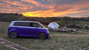 Ein violettes Fahrzeug steht auf einer Wiese, im Hintergrund eine Kuppelstruktur.