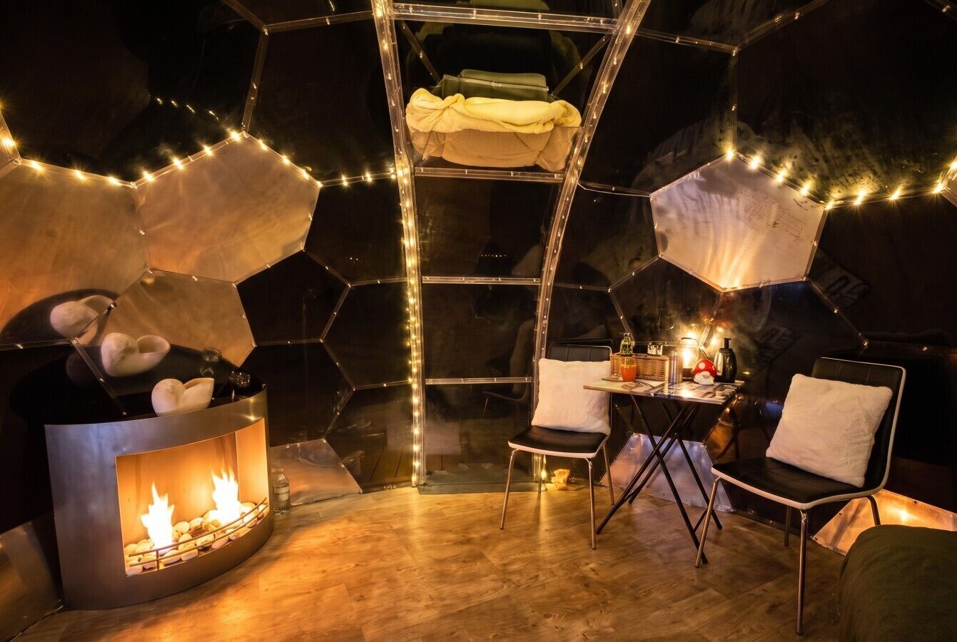 A room with a hexagonal wall design, a central seating area with chairs, a small table, and a fireplace with visible flames.