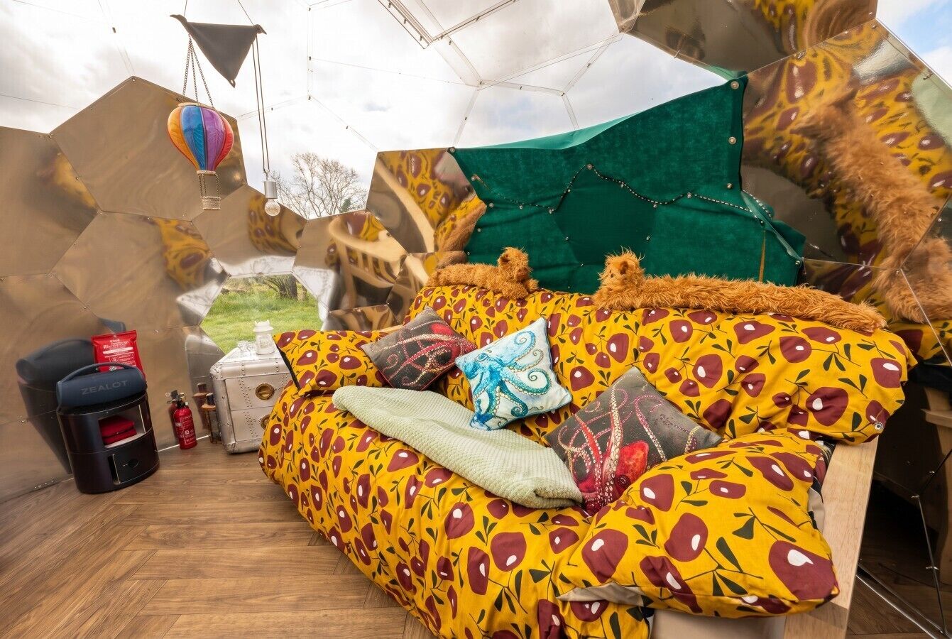 A room with a sofa bed, pillows, a hanging hot air balloon, and a green tent-like structure.