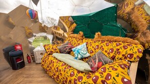 Ein Zimmer mit Schlafsofa, Kissen, einem hängenden Heißluftballon und einer grünen, zeltartigen Konstruktion.