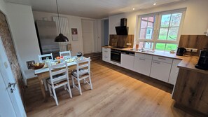 A modern kitchen with white cabinetry, a wooden dining table, and a large window providing a view of the outdoors. - Cozy vacation rental in the picturesque town of Uehrde (Osterode am Harz)