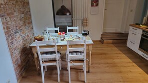 A dining area with a brick wall, a wooden table, white chairs, and a hanging pendant light. - Cozy vacation rental in the picturesque town of Uehrde (Osterode am Harz)