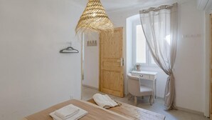 Ein Zimmer mit Holztisch, einer Pendelleuchte, einem Schreibtisch mit Stuhl und einem fenster mit Vorhängen.