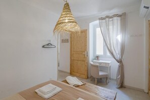 A room with a wooden table, a hanging light fixture, a desk with a chair, and a window with curtains. - GuestHost - Azurea Home: Lovely & Spacious Apartment for 6 (Sanremo)