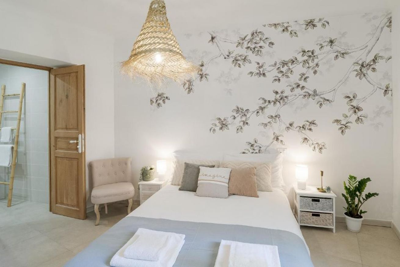 Un dormitorio con cama, mesitas de noche, una silla, lámpara colgante y un mural en la pared.