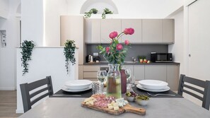 A dining table set with a variety of cheeses, cured meats, and olives, accompanied by a bottle of wine and a vase with flowers. - Italianway Comfort - Cellini 1 (Milan)