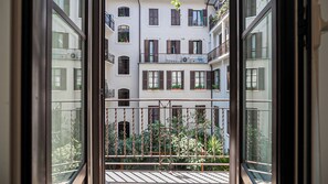 A view through a window of a multi-story building with balconies, potted plants, and a metal railing. - Italianway Comfort - Cellini 1 (Milan)