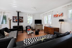 Una sala de estar con un sofá negro, un televisor, una chimenea y obras de arte en las paredes.
