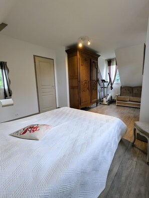 A bedroom with a large bed, a wardrobe, a bench, and a window with curtains.