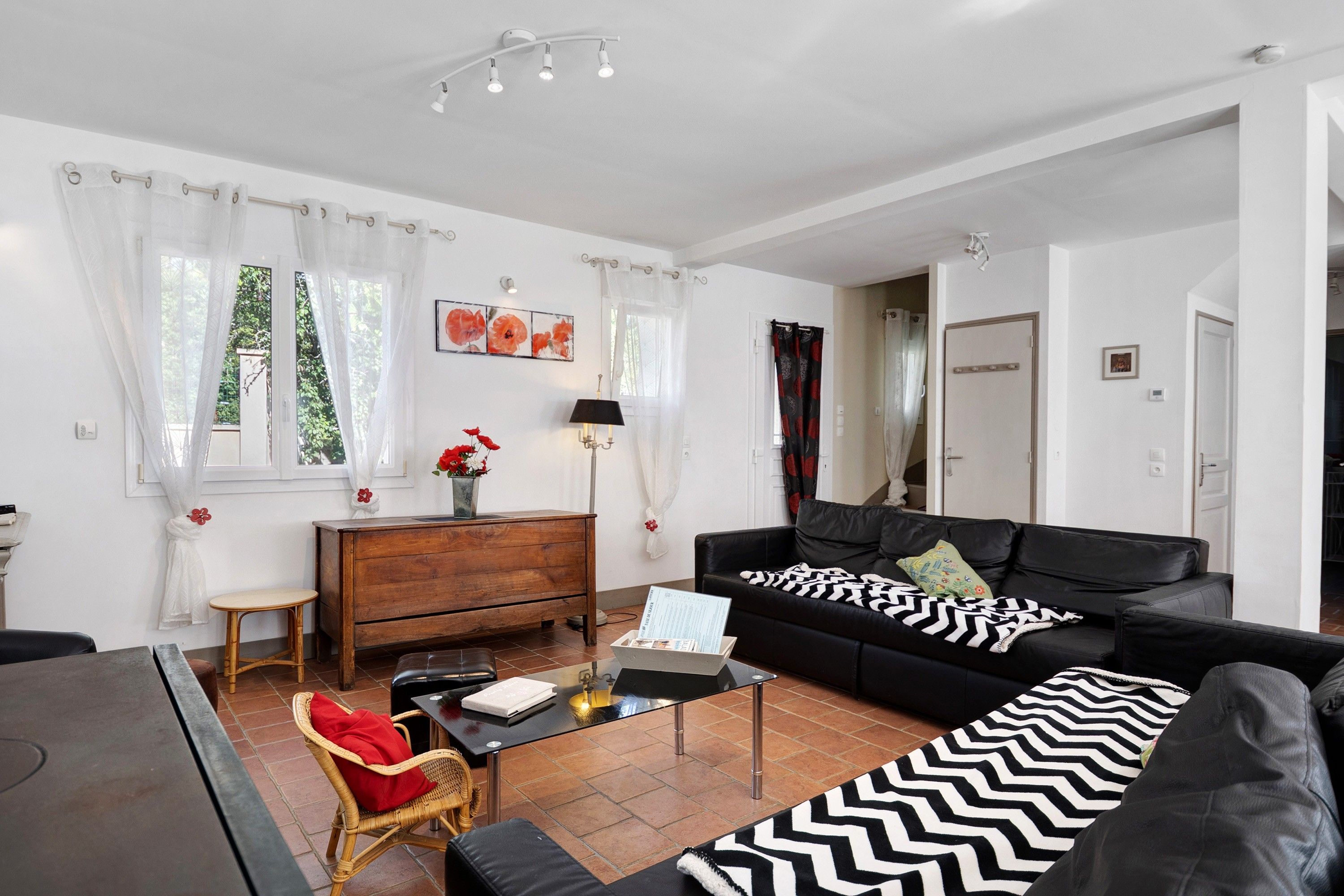 Un salon moderne avec un canapé en cuir noir, une table basse en bois, un fauteuil en osier et une table à manger.