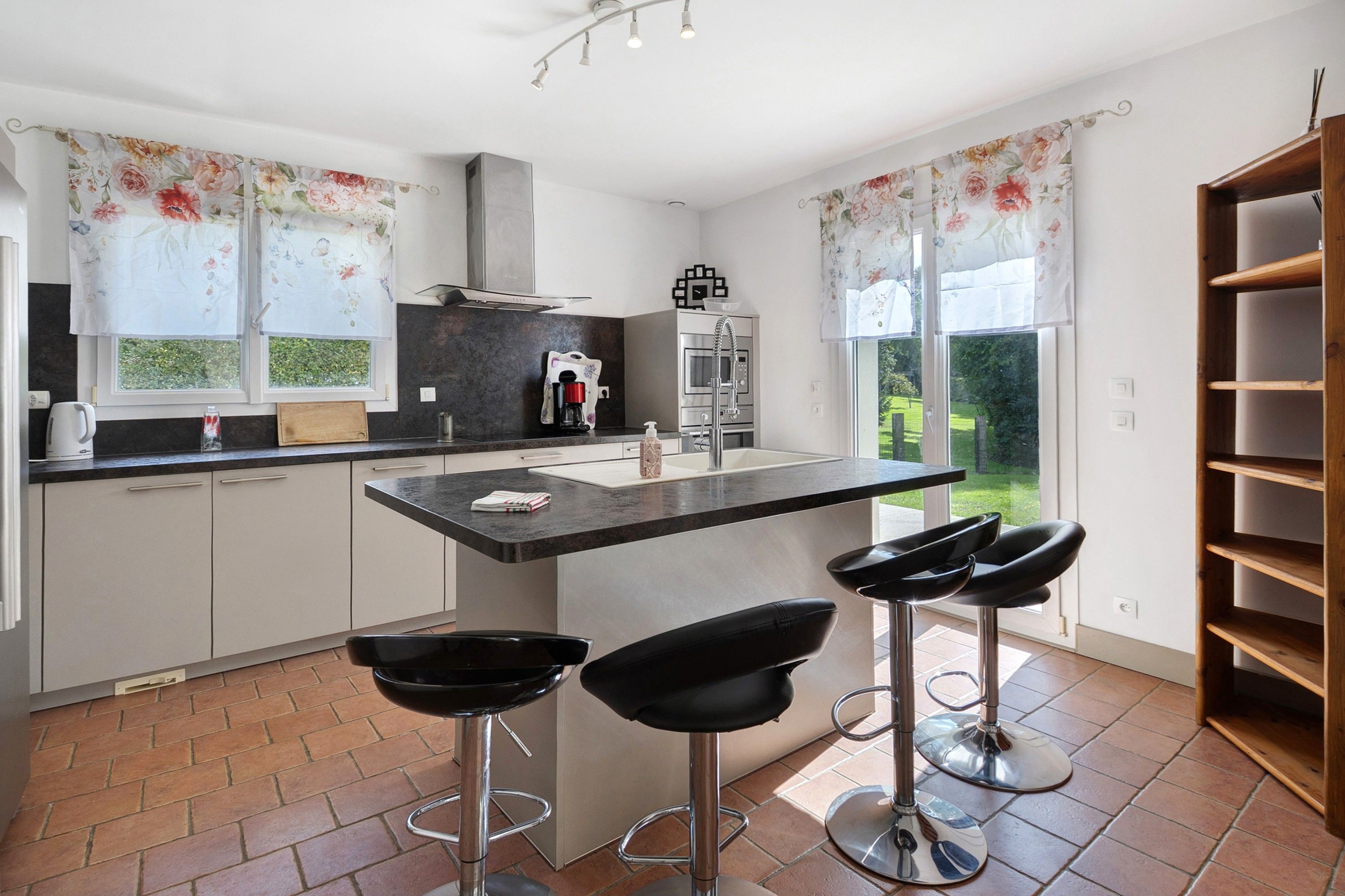 Eine moderne Küche mit einer zentralen Kochinsel, Barhocker und Blick zum Garten.