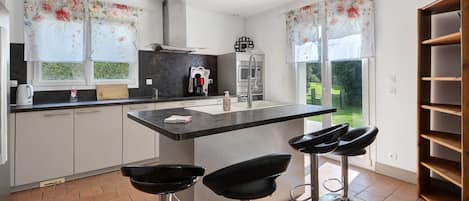 A modern kitchen with a central island, bar stools, and a view of the garden.