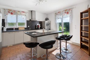 Een moderne keuken met een centraal eiland, barstoelen en uitzicht op de tuin.