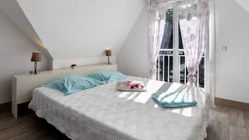 A bedroom with a sloped ceiling, a bed with a white quilt and blue pillows, two bedside lamps, and a window with floral curtains.