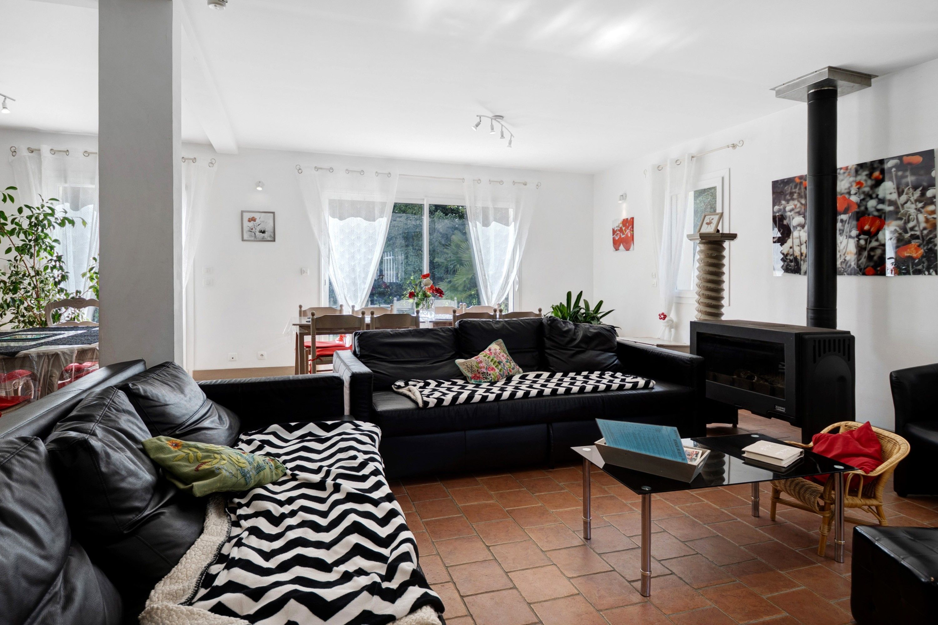 A living room with a black leather sofa, a black and white striped throw, a fireplace, and a large window with sheer curtains.