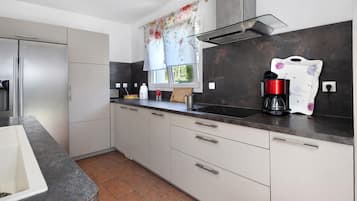 A modern kitchen with a built-in oven, a coffee maker, and a window with floral curtains.
