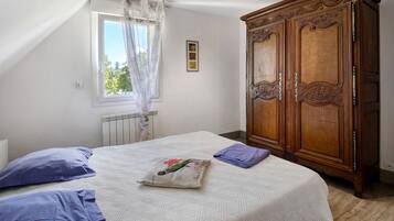 A bedroom with a bed, a radiator, a window with curtains, and a wooden wardrobe.