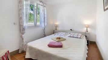 A bedroom with a bed, two bedside lamps, a window with curtains, and a door.