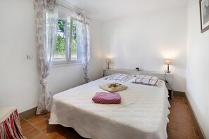 Un dormitorio con una cama, dos lámparas de noche, una ventana con cortinas y una puerta.