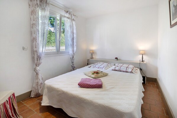 Un dormitorio con una cama, dos lámparas de noche, una ventana con cortinas y una puerta.