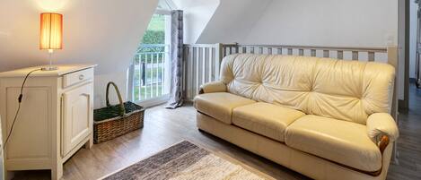 Una habitación con un sofá blanco, una lámpara, una cesta de mimbre y vistas al exterior con vegetación.