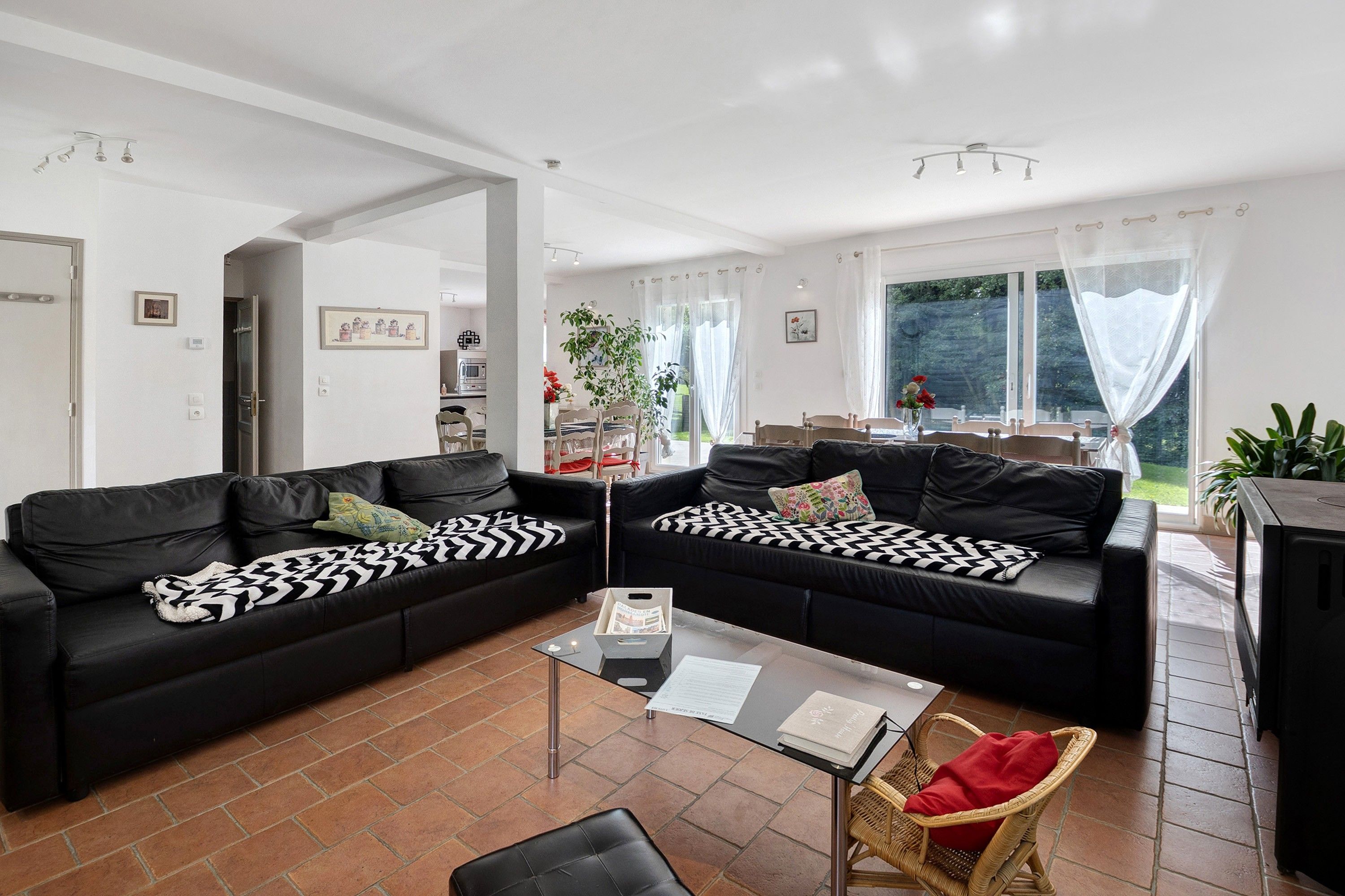 Ein modernes Wohnzimmer mit zwei schwarzen Ledersofas, einem Glastisch und einem Korbstuhl.