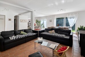 Een moderne woonkamer met twee zwarte leren banken, een glazen salontafel en een rieten fauteuil.