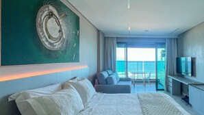 A modern hotel room with a large bed, a TV, and a balcony with a view of the sea. - Beachfront w/ an amazing rooftop - Prime location (Salvador)