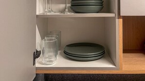 A kitchen cabinet with shelves containing clear glassware, green plates, and a clear bowl. - Beachfront w/ an amazing rooftop - Prime location (Salvador)