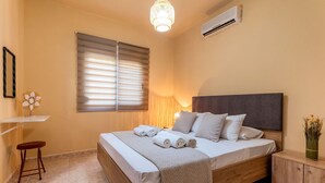 Ein Schlafzimmer mit Bett, Nachttisch, Lampe und einer Wand-Klimaanlage.