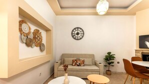 Ein Wohnzimmer mit einer Couch, zwei runden Tischen, einer Wanduhr, Wanddekoration und einem Topfpflanzen.