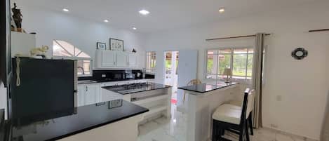 A modern kitchen with a central island, white cabinetry, and a dining area with a chair.
