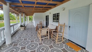 Eine überdachte Veranda mit einem gemusterten Boden, Holzmöbeln und einer weißen Tür.