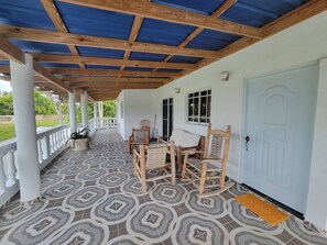 A covered porch with a patterned floor, wooden furniture, and a white door. - Villa Tropical - Penthouse 10 (Sosúa)