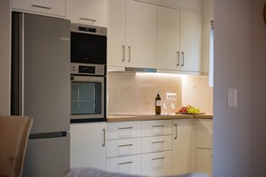 A modern kitchen with white cabinetry, a built-in oven, and a wine bottle on the counter. - Villa Idola Dassia Corfu (Dassia)