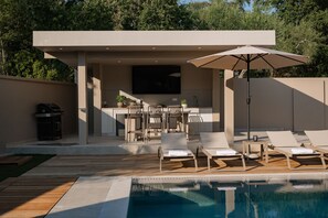 A modern outdoor pool area with lounge chairs, a barbecue grill, and a flat-screen TV. - Villa Idola Dassia Corfu (Dassia)