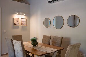 A dining area with a wooden table, four chairs, a vase with flowers, and three wall-mounted mirrors. - Villa Idola Dassia Corfu (Dassia)