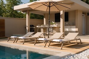 Ein Poolbereich mit Liegestühlen, einem Sonnenschirm, einem Grill und einer Küchenzeile.