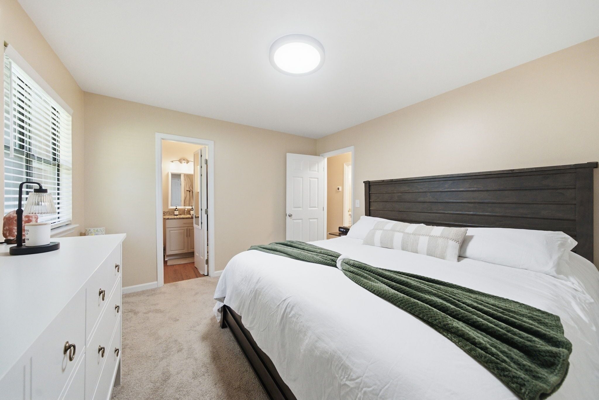A bedroom with a bed, a dresser, a mirror, and a door leading to a bathroom.