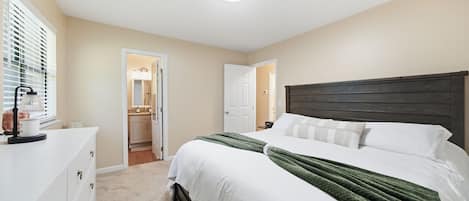 A bedroom with a bed, a dresser, a mirror, and a door leading to a bathroom.