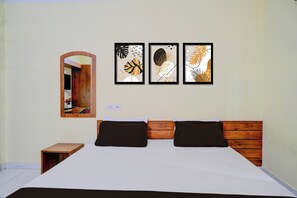 Un dormitorio con cabecera de madera, cama con ropa de cama blanca, dos almohadas negras y tres cuadros en la pared.