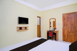 Una habitación de hotel con cama, escritorio, televisión, espejo y armario.