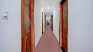 A long, narrow hallway with wooden doors on both sides and a red carpet. - Super Collection O Bashista Chariali (Guwahati)