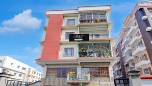 A multi-story residential building with a company-serviced sign, balconies with potted plants, and a garage entrance. - Super Collection O Bashista Chariali (Guwahati)